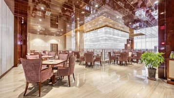 A spacious hotel lobby with a high ceiling, polished floors, and a central seating area with tables and chairs.