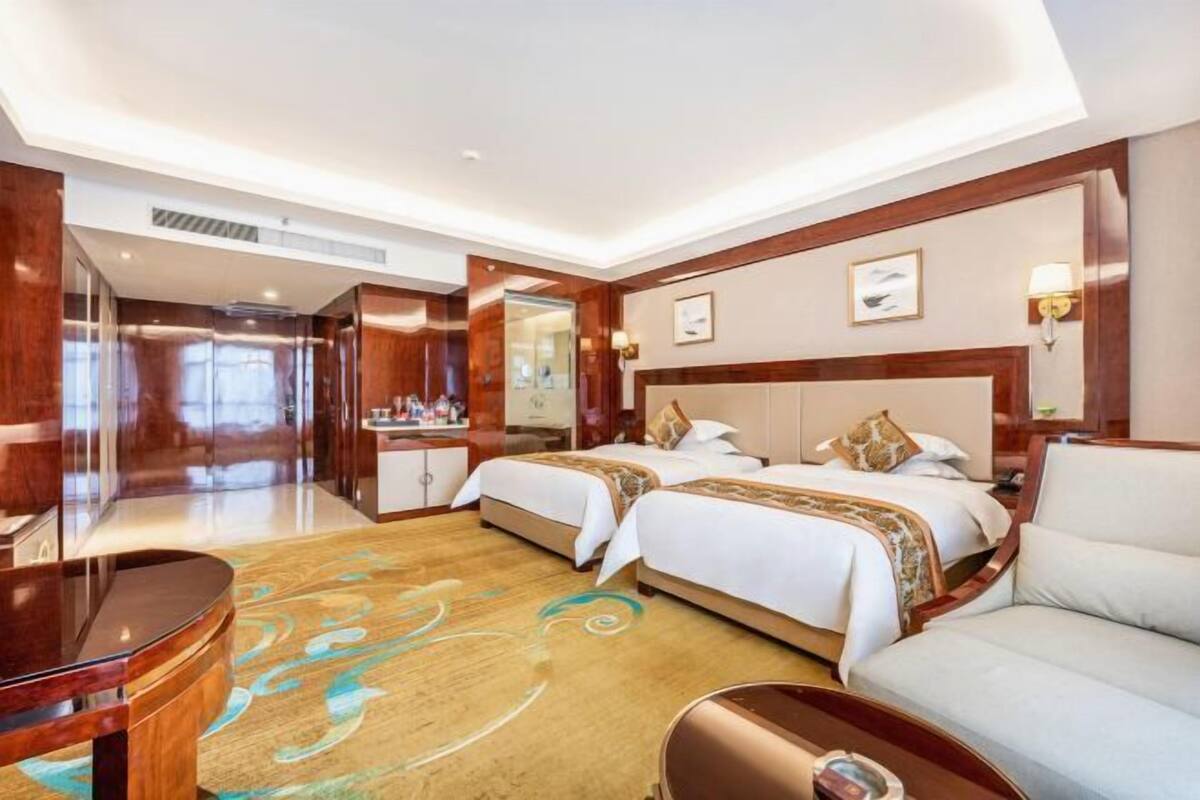 A hotel room with two beds, a sitting area, a desk, and a bathroom.