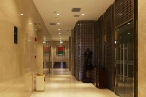 A hotel corridor with a tiled floor, a trash bin, and a glass door on the right. - Xixia International Hotel (Cheng County)