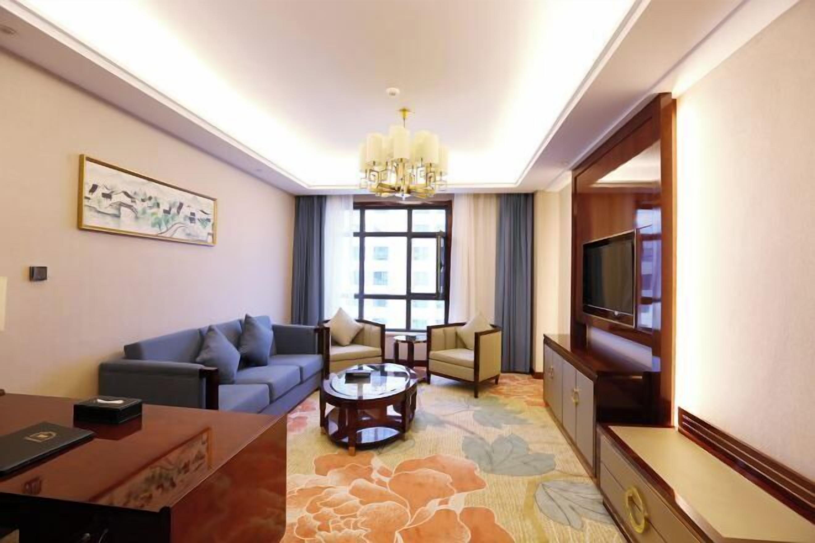 Una sala de estar con sofá, sillones, una mesa de centro, televisor y candelabro.