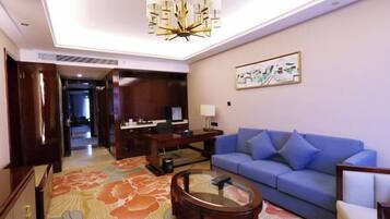 Habitación de hotel con sofá azul, una mesita de centro redonda, un escritorio con computadora y una alfombra grande con estampado floral.