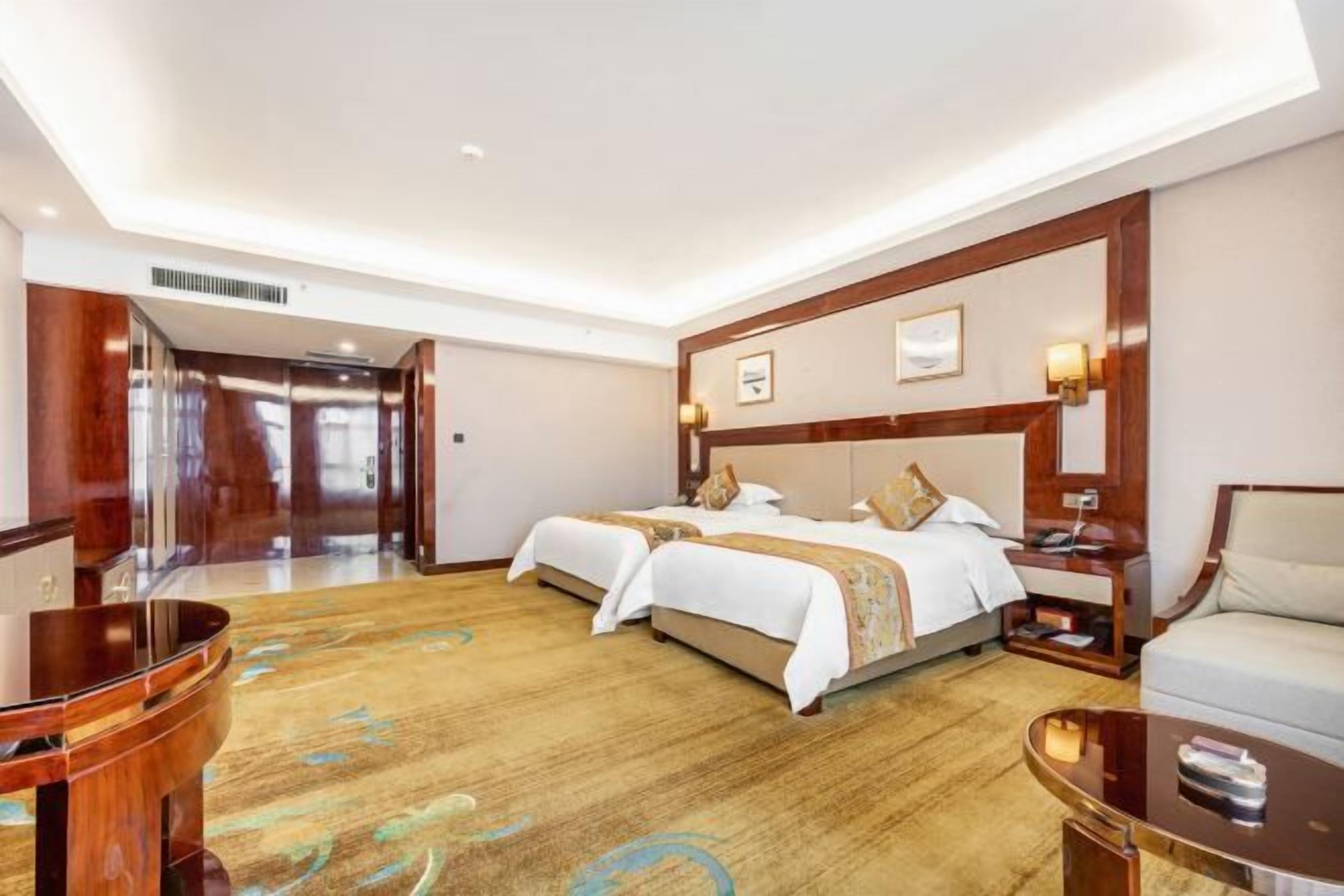 Ein Hotelzimmer mit zwei Betten, einem Holztisch, einem Stuhl und Teppichboden.