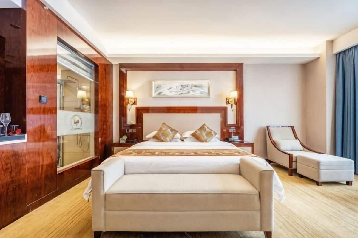 A hotel room with a large bed, a sitting area, a mirror, and a painting on the wall.