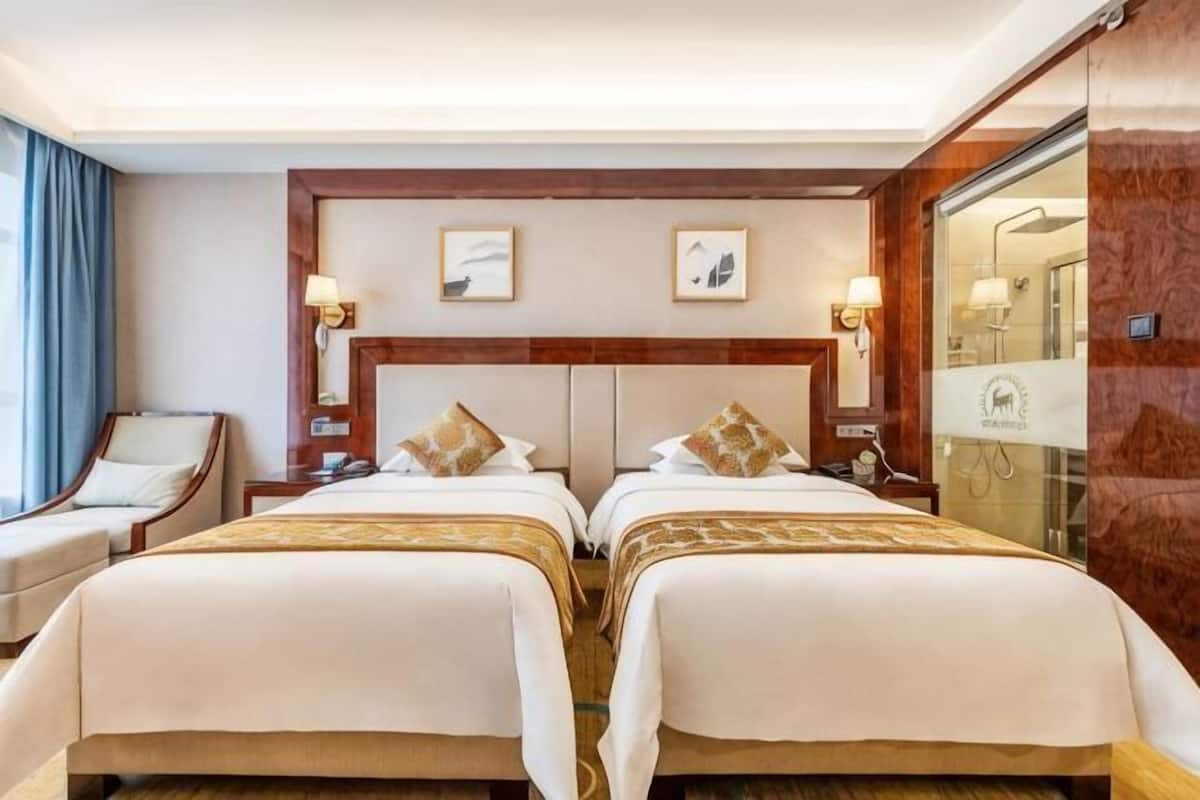 A hotel room with two beds, a sitting area, a bathroom, and a view of the city.