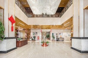 Un vestíbulo espacioso con techo alto, una recepción y una fuente decorativa en el centro.