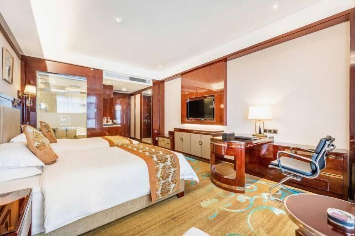 A hotel room with a large bed, a desk with a chair, a television, and a bathroom visible through an open door.