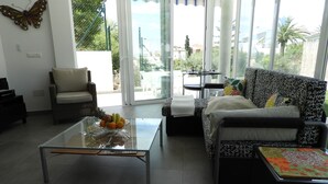 A living room with a glass coffee table, a sofa, a chair, and a view of the outdoors through large windows.