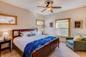 A bedroom with a bed, a nightstand, a lamp, a chair, and a ceiling fan.