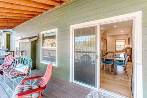 A covered deck with outdoor furniture, a sliding glass door leading to an interior dining area, and a view of the outdoors.