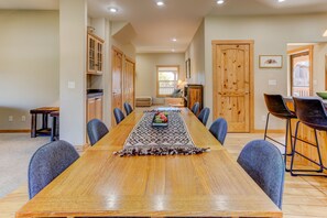 A long dining table with a fruit bowl centerpiece, surrounded by chairs, in a room with wooden cabinets and a fireplace.