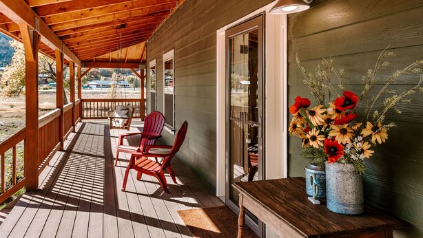 A wooden porch with a covered area, two chairs, a table, and a vase with flowers. - Animas River House - 22 acres of Riverfront with Amazing Views-20 mins to skiing (Durango)