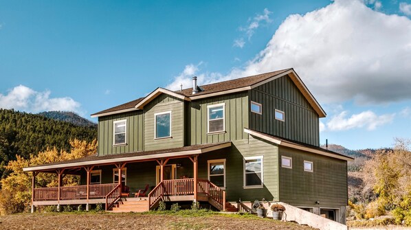 A two-story house with a porch, a chimney, and a view of a forested mountain.