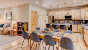 A modern kitchen with wooden cabinets, a central island, and a dining area with a table and chairs. - Animas River House - 22 acres of Riverfront with Amazing Views-20 mins to skiing (Durango)