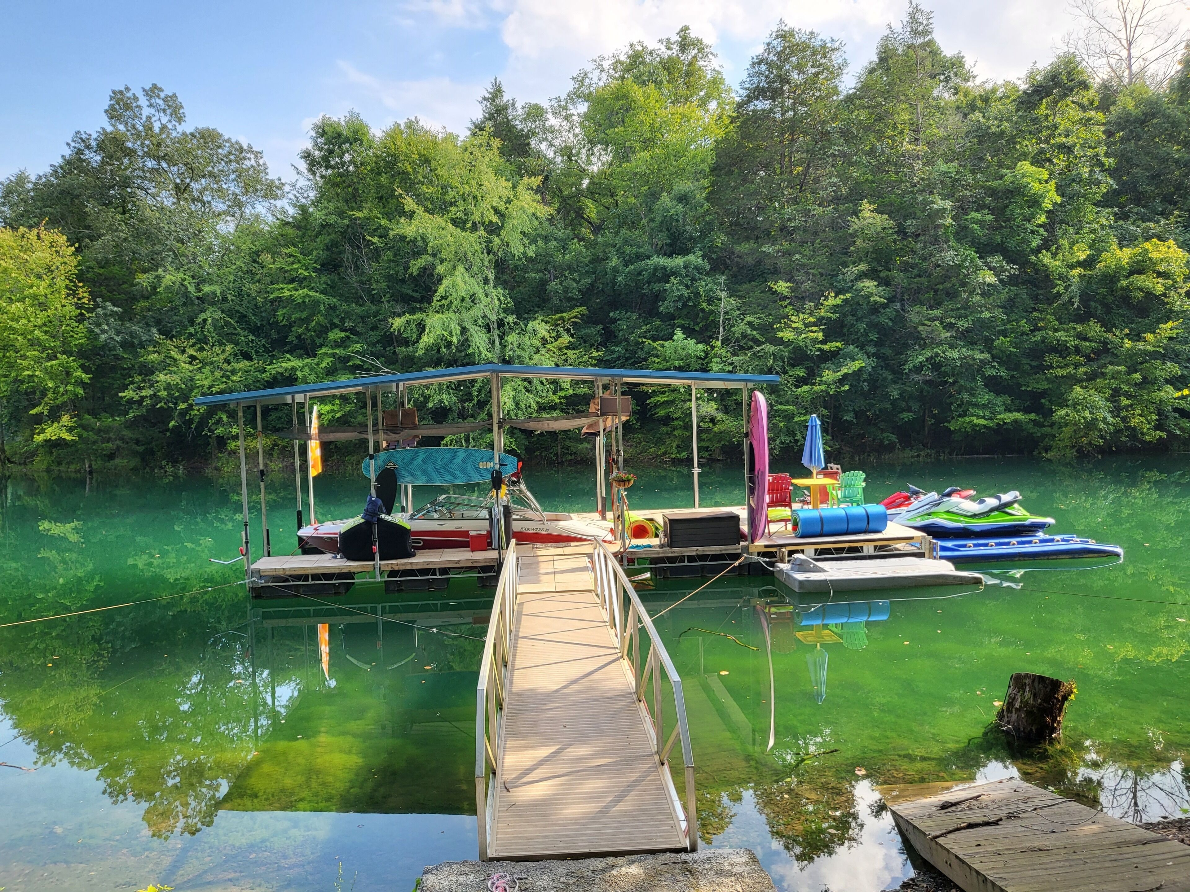 A dock with a covered seating area, a boat, and a floating platform with chairs and a table.