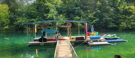 A dock with a covered seating area, a boat, and a floating platform with chairs and a table.