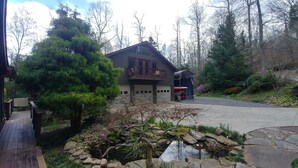Een tweelaags huis met garage, omringd door bomen en een klein vijvertje.