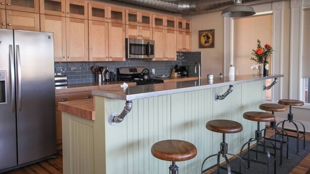 Une cuisine dotée de meubles en bois, d’appareils électroménagers en acier inoxydable, d’un îlot central avec des tabourets et d’un luminaire suspendu.