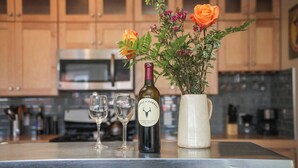 Un comptoir de cuisine avec une bouteille de vin, deux verres à vin et un vase rempli de fleurs.
