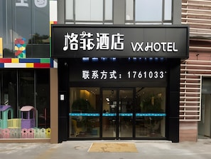 A hotel entrance with a sign displaying the name 'VX Hotel' and a contact number.