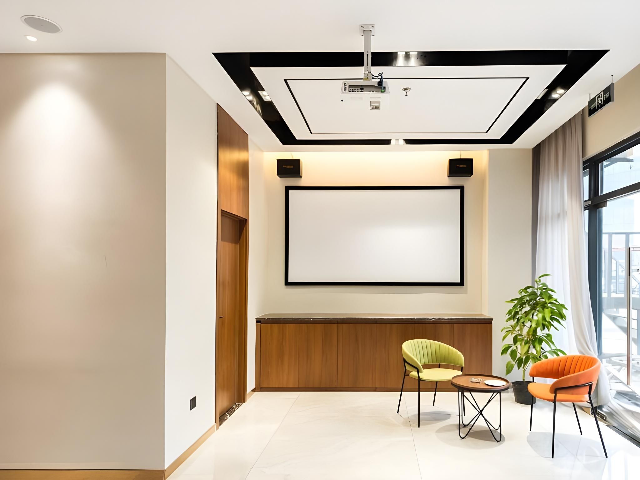 A conference room with a large screen, two chairs, a small table, and a potted plant.