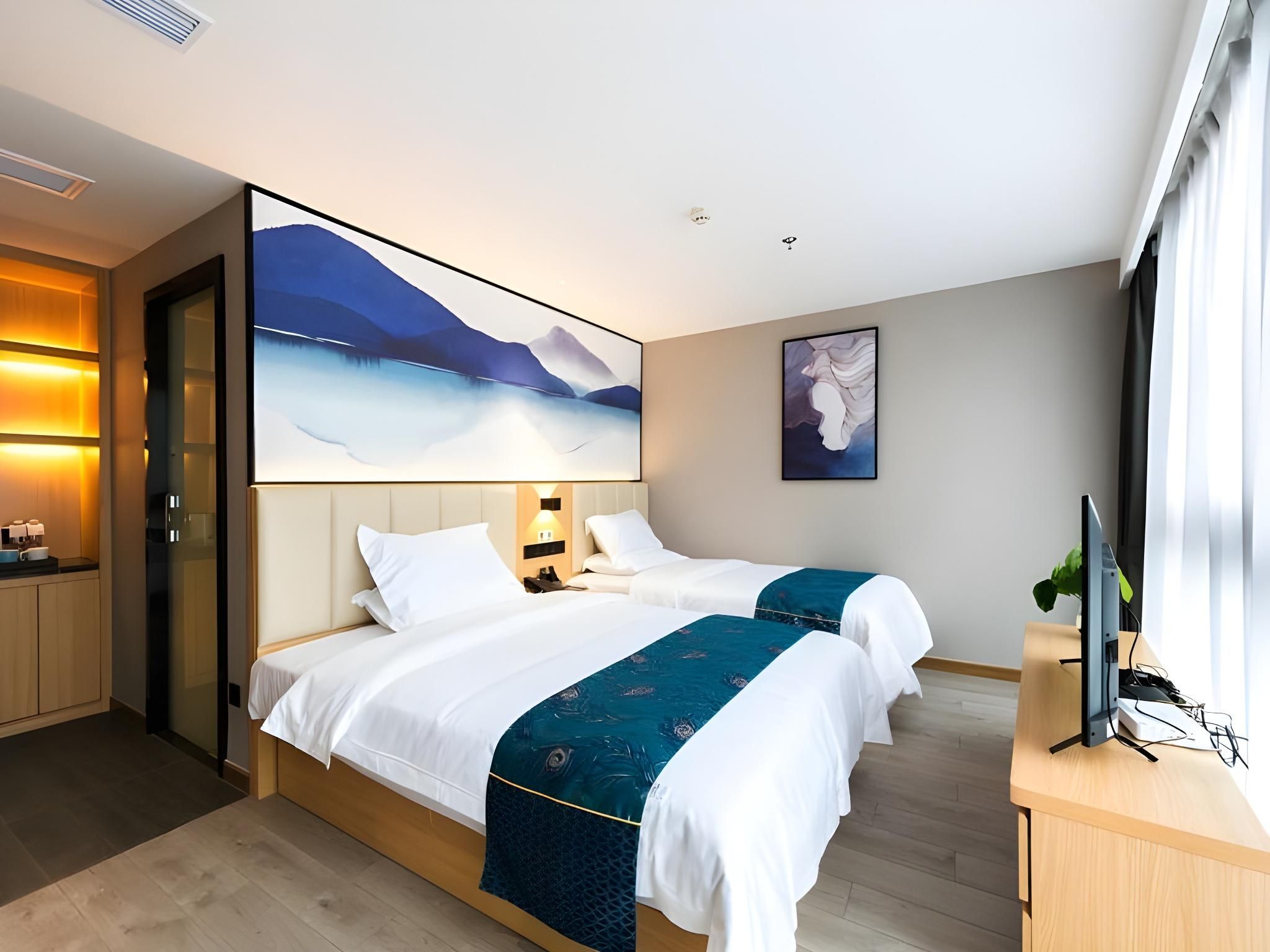 A hotel room with two beds, a desk, a large window, and artwork on the walls.