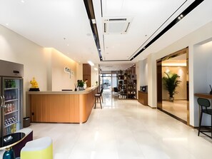 A modern hotel lobby with a reception desk, a seating area, and a plant.