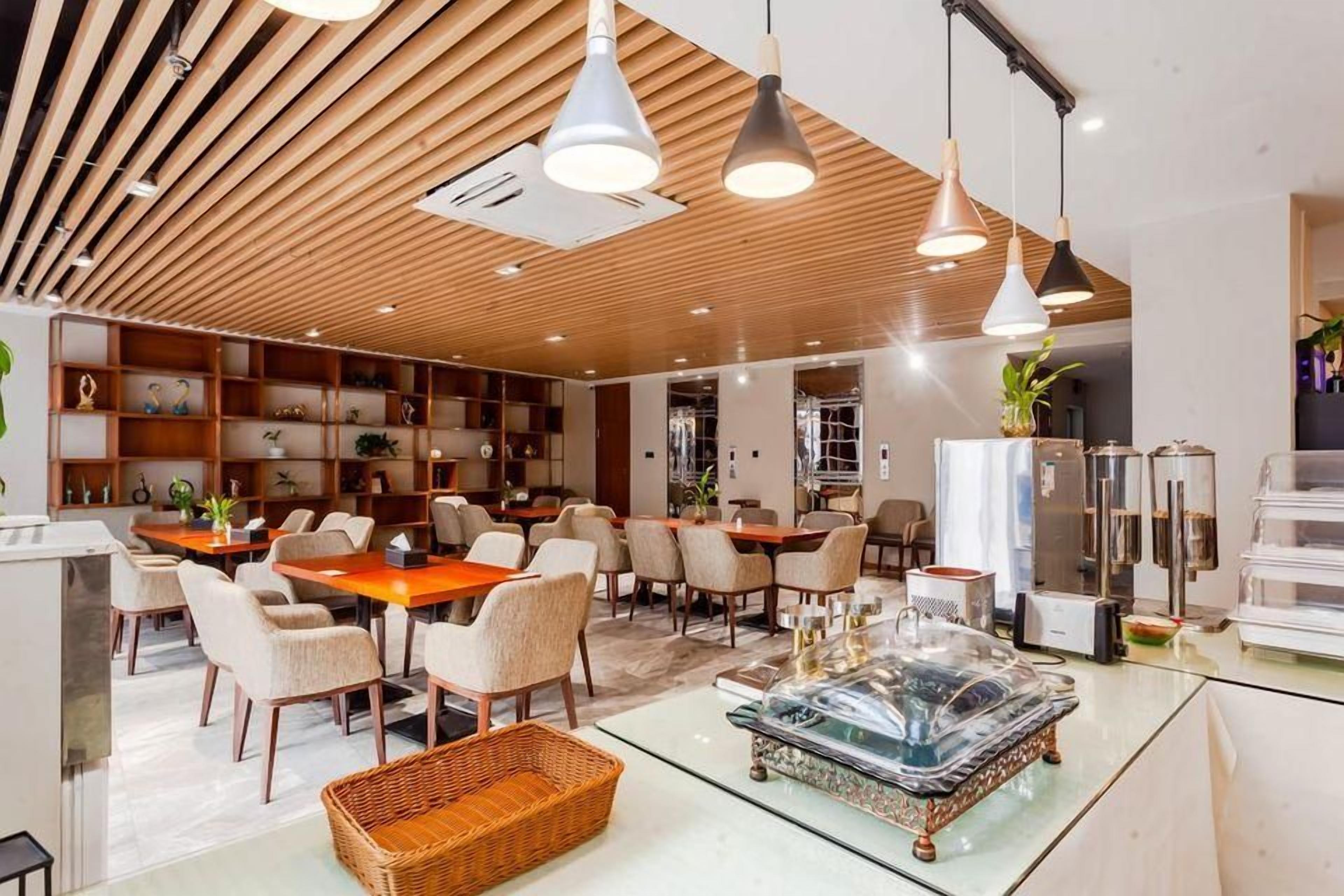 A modern hotel lobby with wooden ceiling panels, multiple dining tables, and chairs.