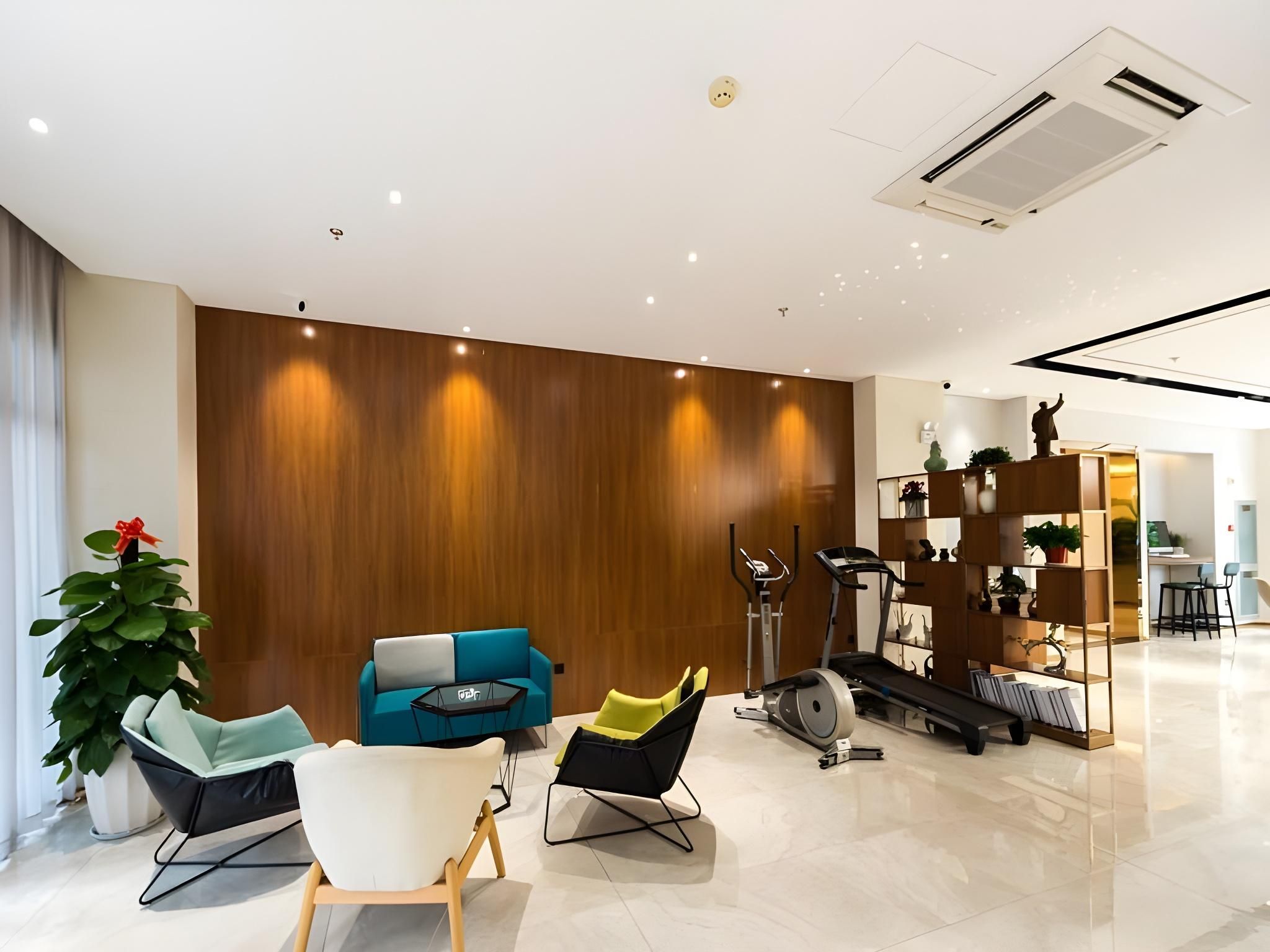 A modern living room with a wooden accent wall, a blue sofa, a white armchair, a yellow chair, and a treadmill.