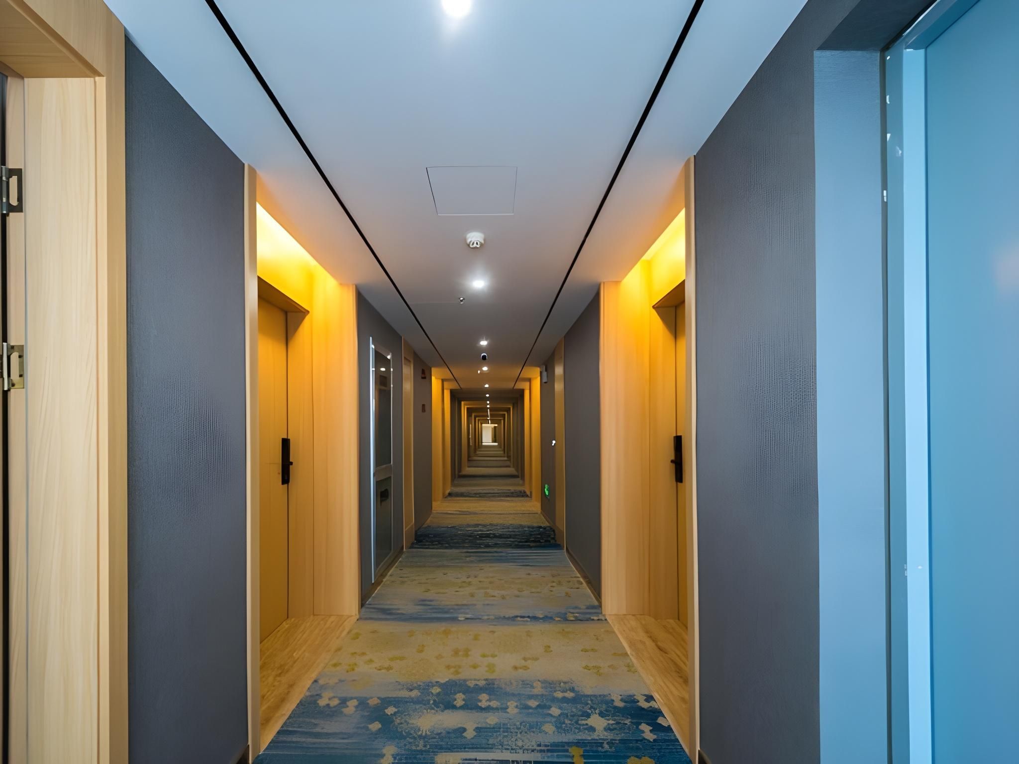 A hotel hallway with a carpeted floor, wooden doors, and recessed lighting.
