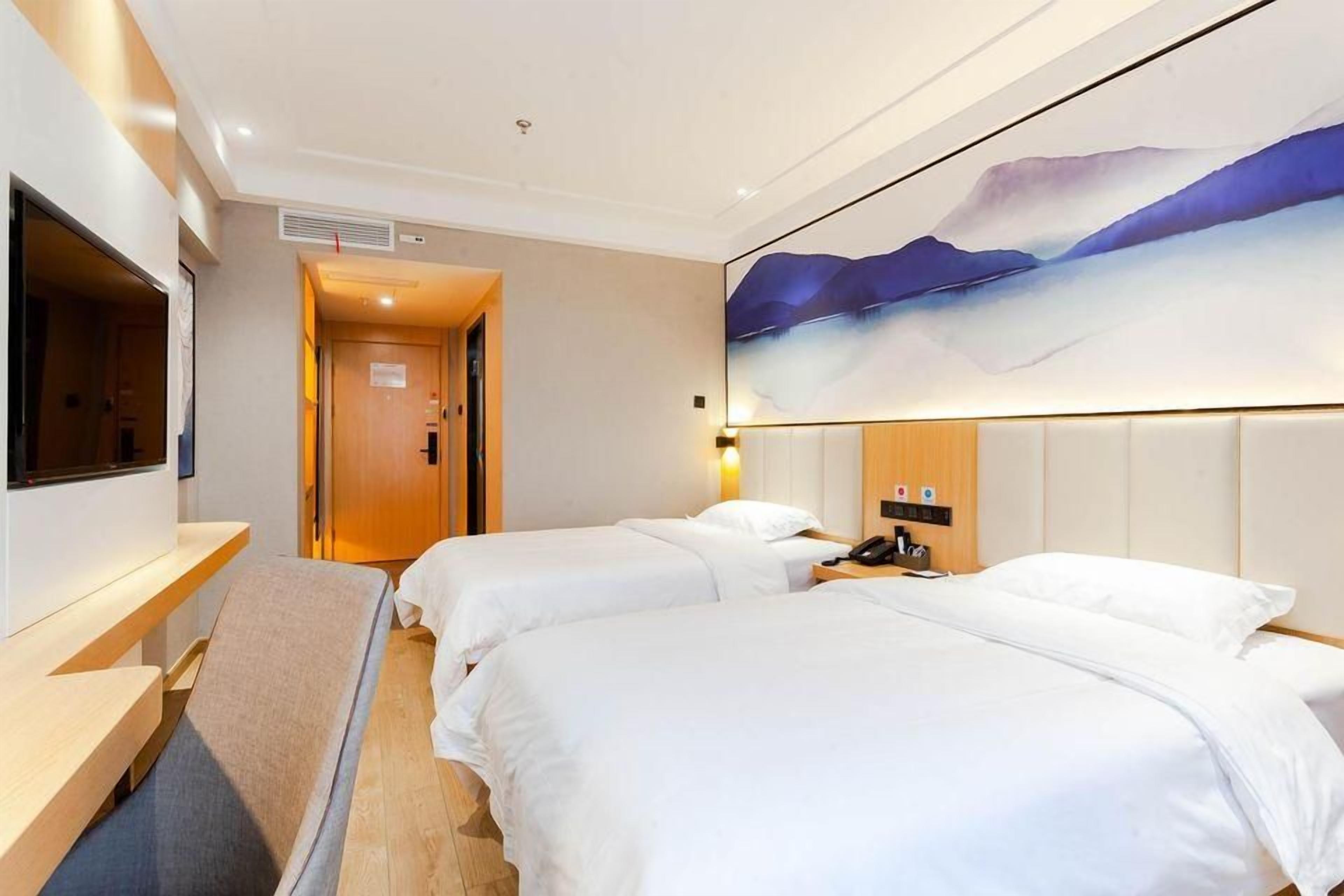 A hotel room with two beds, a desk, a TV, and a painting on the wall.