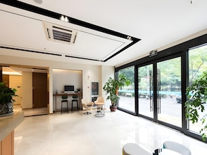 Un interior moderno con un mostrador de recepción, zona de estar y grandes ventanales con vistas al exterior.