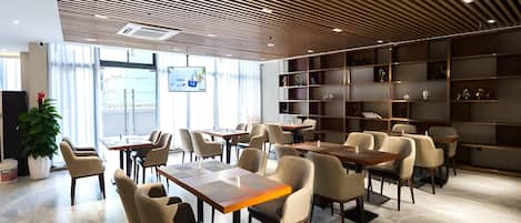 A modern interior with a wooden slatted ceiling, multiple seating areas with tables, and a large bookshelf.