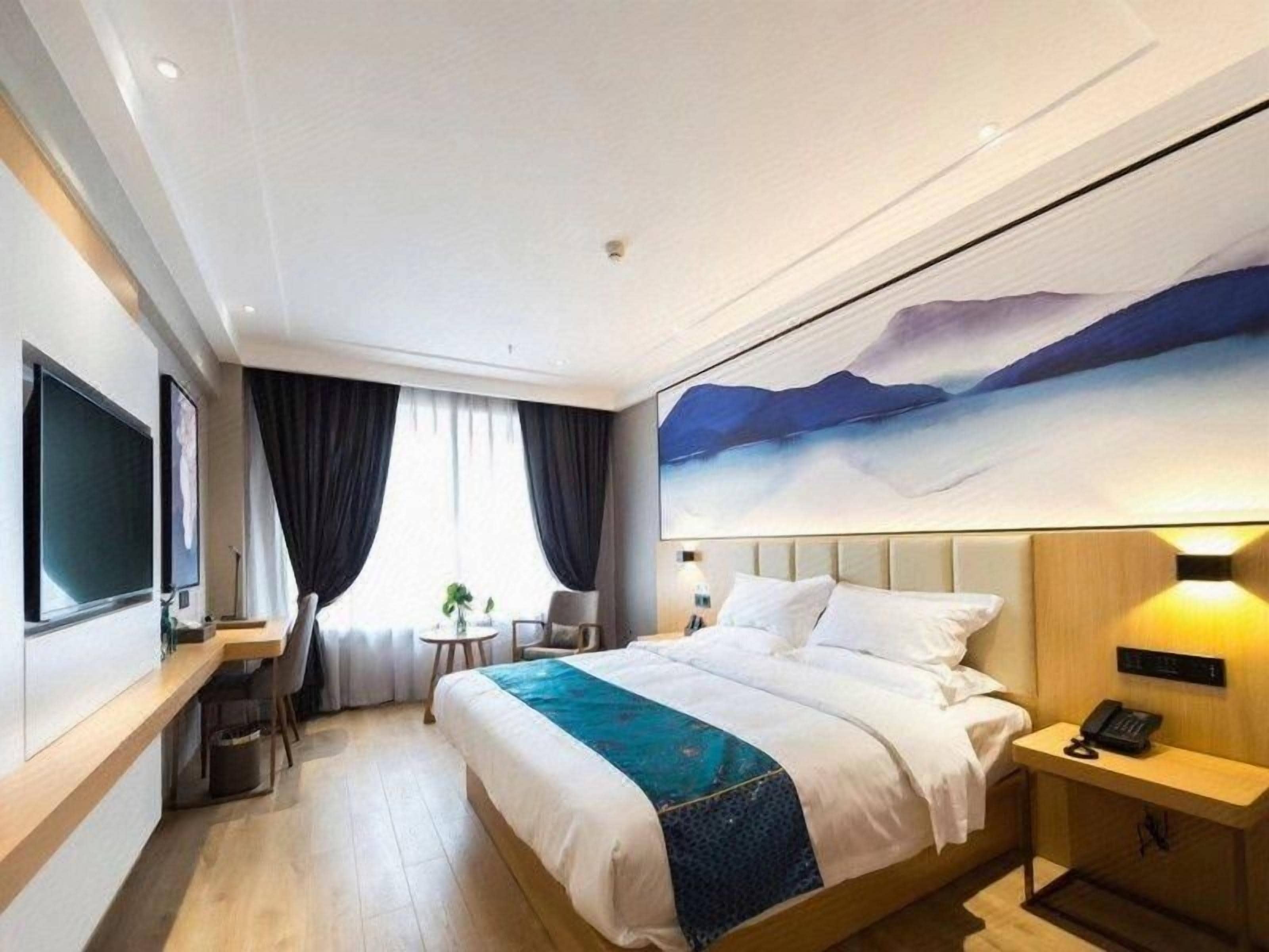 A hotel room with a bed, bedside table, lamp, and a large painting on the wall.