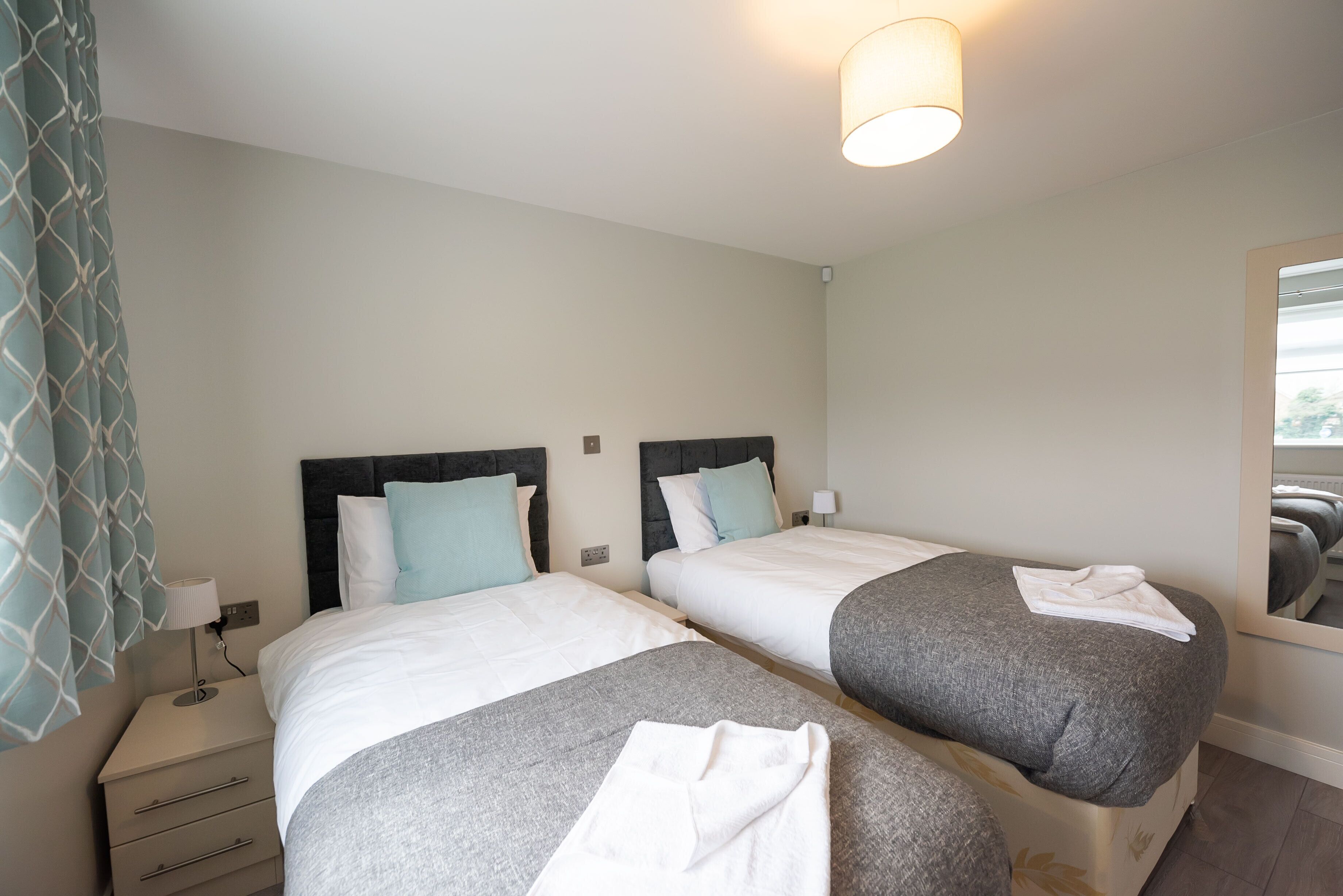 A hotel room with two beds, a nightstand, a lamp, and a mirror.