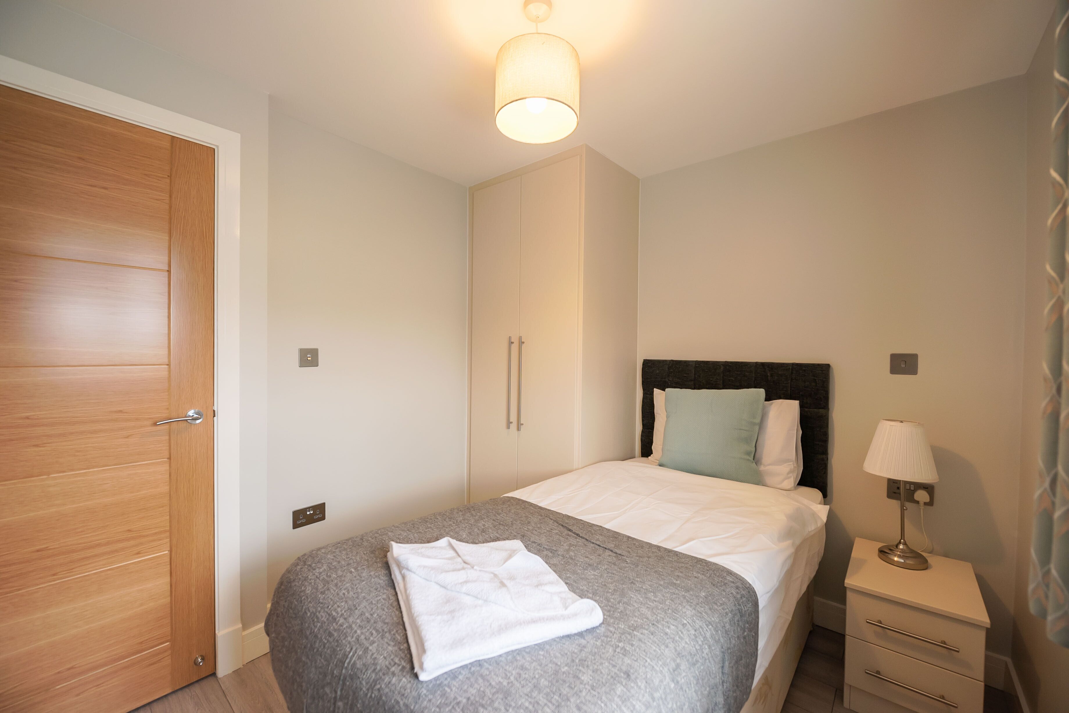 A bedroom with a bed, a nightstand, a lamp, a wardrobe, and a ceiling light.