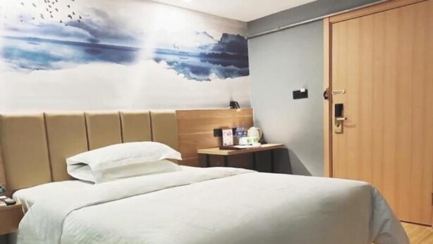A hotel room with a bed, a bedside table, a nightstand, a wall mural, and a wooden door. - Greentree Inn Taiyuan Hanxiguan Street Wanda Mansion Shell Hotel (Taiyuan)
