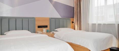 Une chambre d’hôtel avec deux lits, une tête de lit en bois, une table de chevet et une fenêtre avec des rideaux légers.