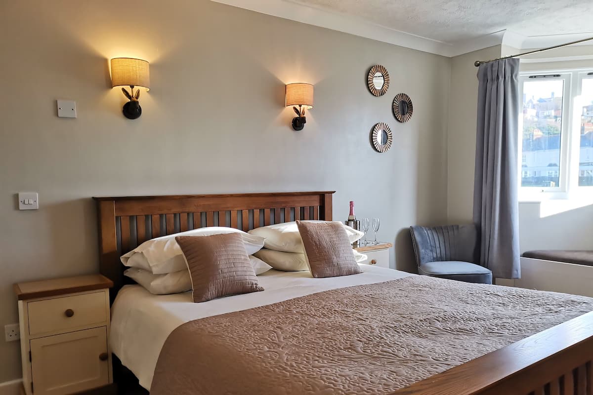 A neatly made bed with a wooden headboard, a bedside table with a lamp, and wall-mounted sconces.