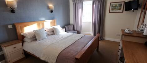 Quarto de hotel com cama de madeira, mesas de cabeceira, cômoda, televisão e janela com cortinas.