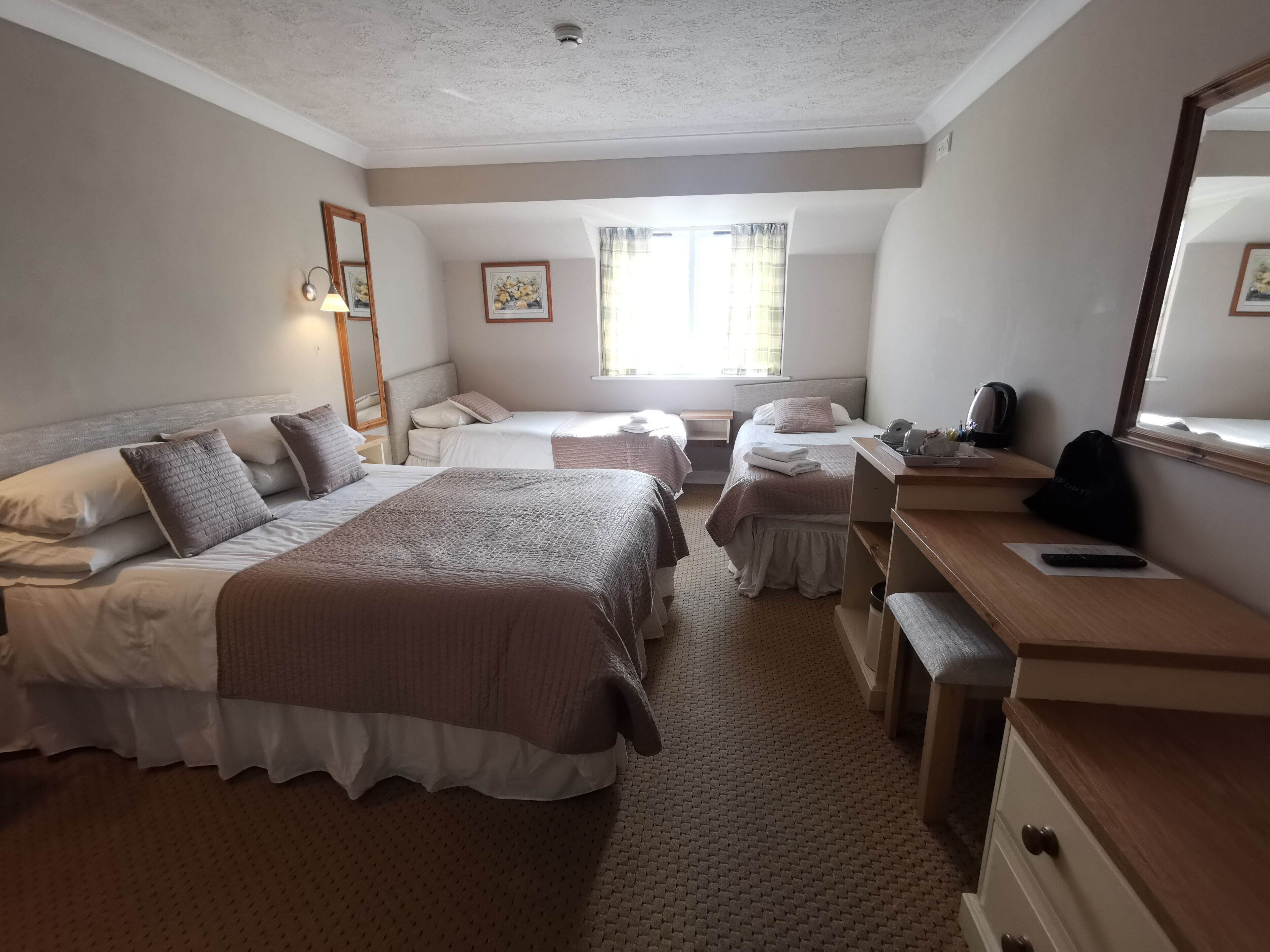 A hotel room with two beds, a desk, a chair, a mirror, and a window.