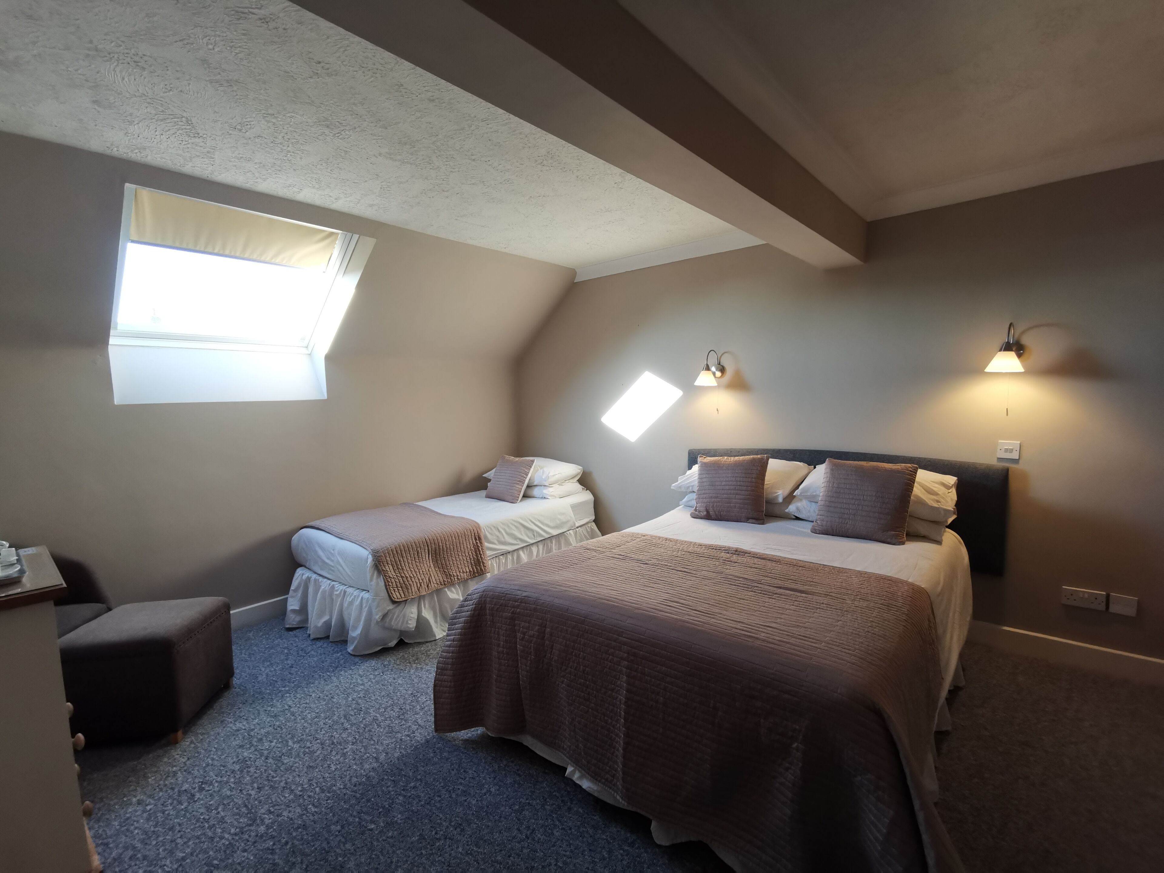 Un dormitorio con dos camas, una ventana e iluminación en la pared.