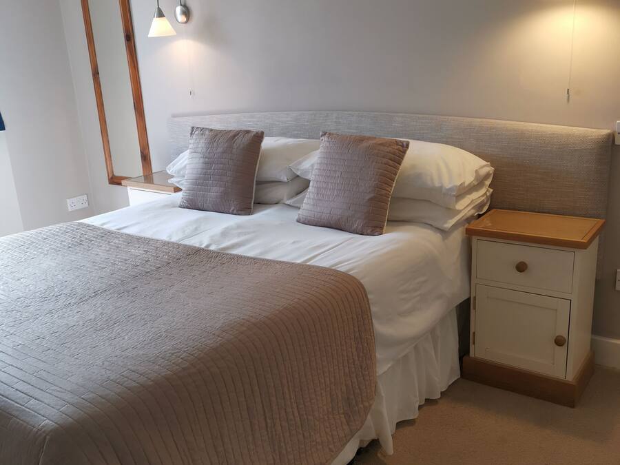 A neatly made bed with a brown quilt, a wooden nightstand with drawers, and two wall-mounted lamps.