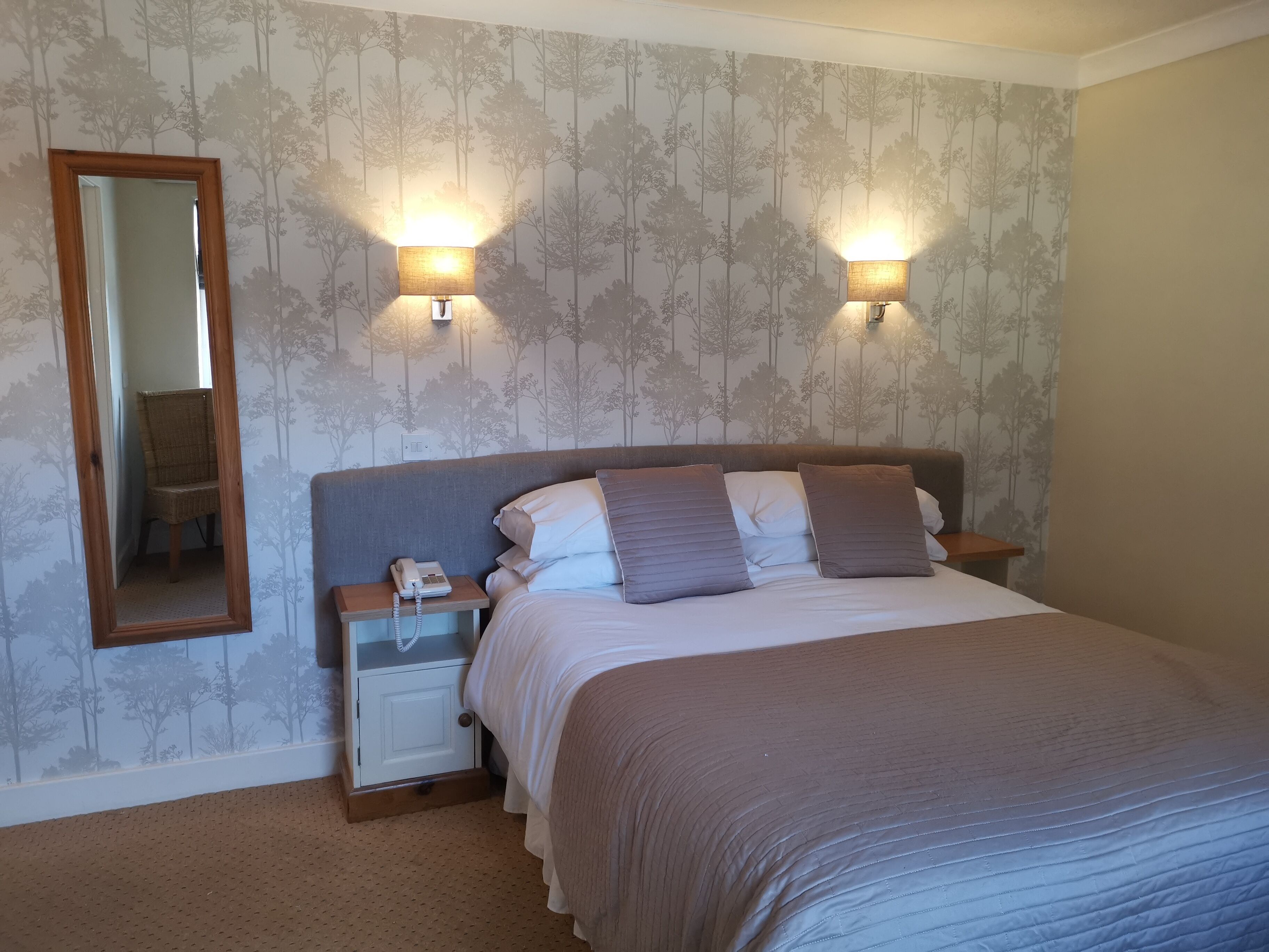 A bedroom with a bed, two bedside lamps, a nightstand with a phone, and a mirror.