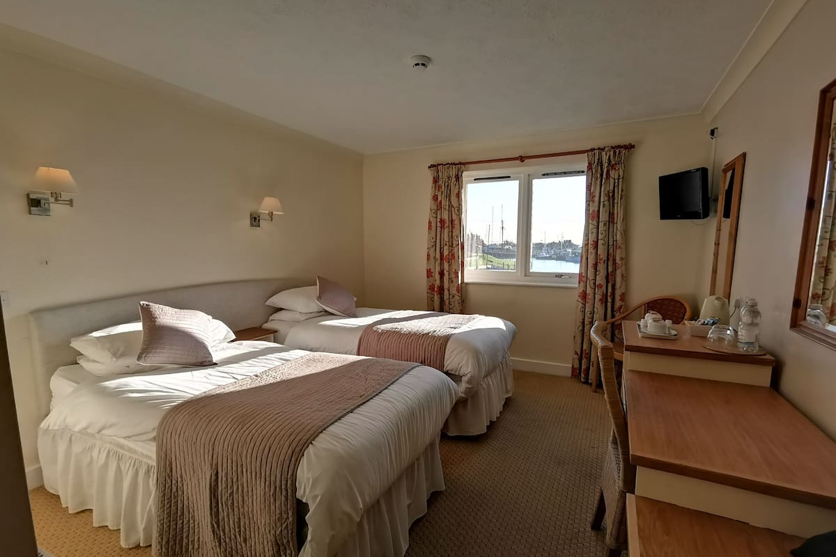 A hotel room with two beds, a desk with a chair, a television, and a window with curtains.