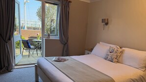 Een hotelkamer met een groot bed, een klein tafeltje, een stoel en uitzicht op de omgeving door een schuifdeur.