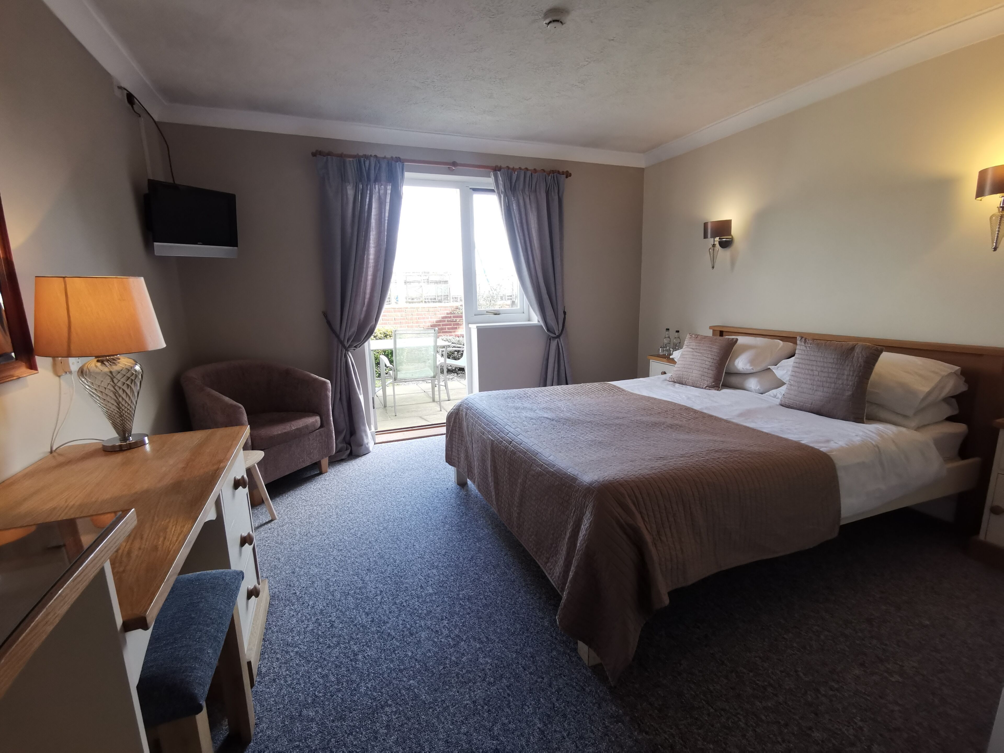 Una habitación de hotel con cama, escritorio, silla, televisor y ventana con cortinas.