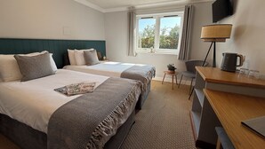 Hotelkamer met twee bedden, een bureau, een stoel, een televisie en een raam met gordijnen.