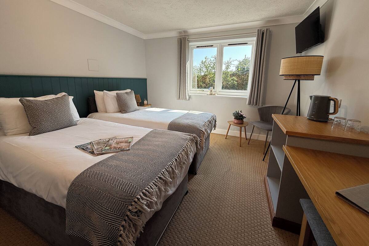 A hotel room with two beds, a desk, a chair, a television, and a window with curtains.