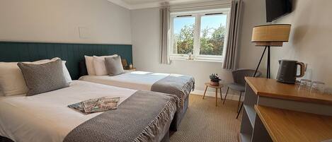 Quarto de hotel com duas camas, uma mesa, uma cadeira, televisão e uma janela com cortinas.
