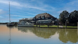 Hotel aan de rivier met restaurant, aangemeerde boten en een voetpad.